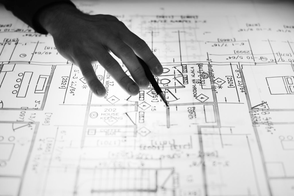 Handing holding pencil while pointing at elements of a blueprint for a house, in black and white